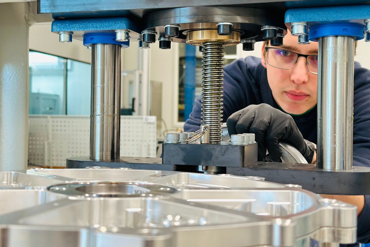 A technician adjusting a precision industrial machine with a threaded spindle and metal components in a workshop.